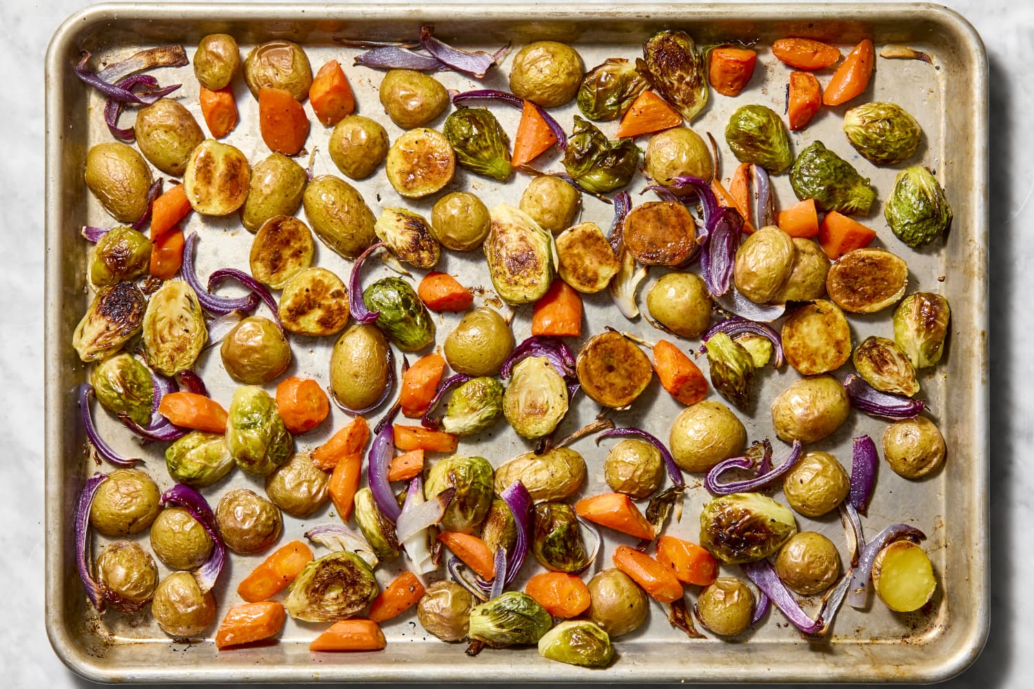 Roasted onions, carrots, potatoes, and brussel sprouts in a sheet pan